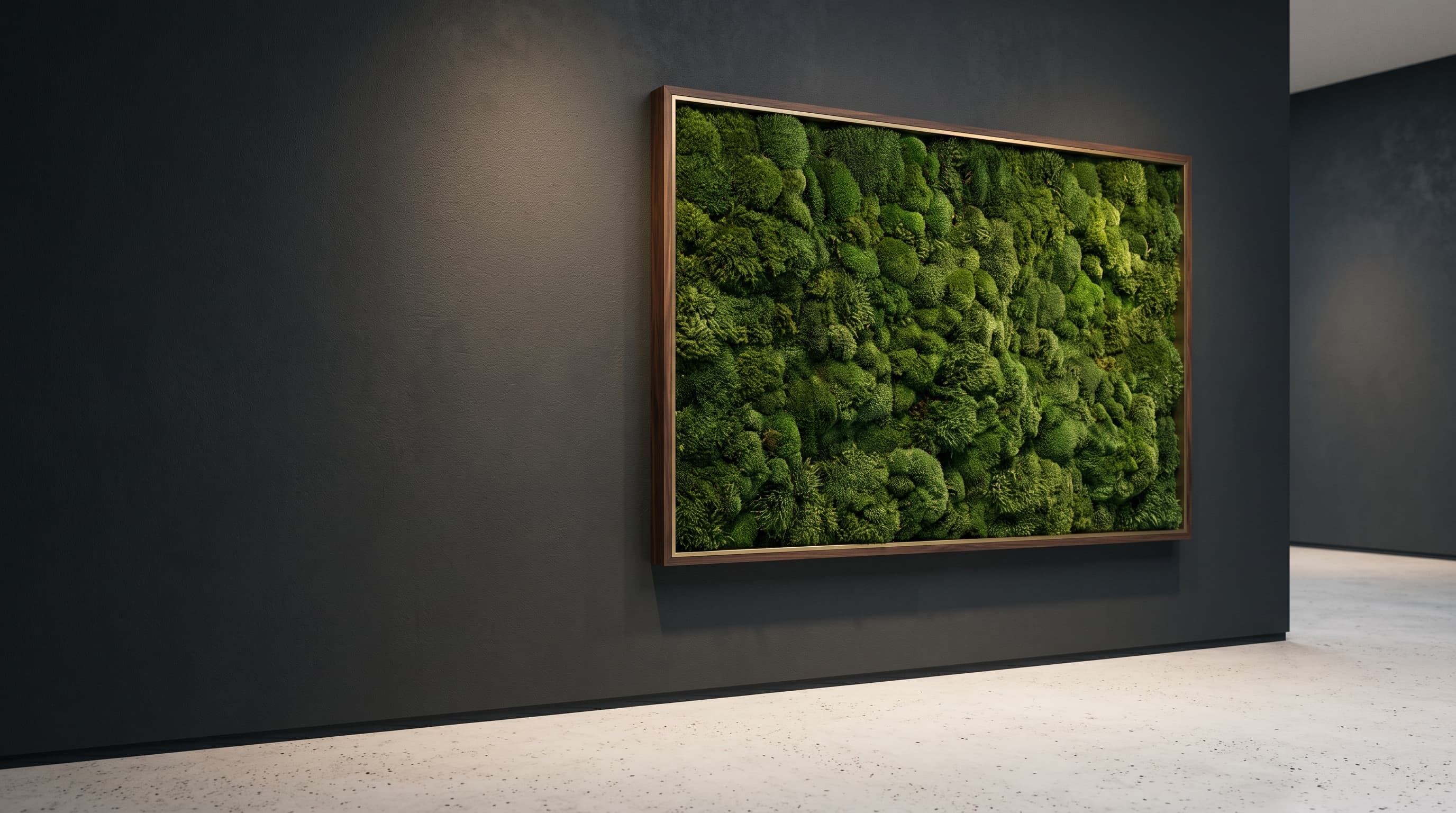 A living moss wall panel in a slim walnut and brass frame, lit by a single museum spotlight against a charcoal gallery wall